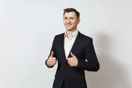 Handsome satisfied caucasian lucky young happy business man 25-30 years in dark suit, light shirt showing thumbs up on white background isolated for advertisementの写真素材