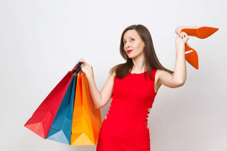 Attractive impressive glamour caucasian fashionable young brown-hair woman in red dress holding beige shoes with red sole, multi colored packets with purchases, shopping isolated on white backgroundの写真素材