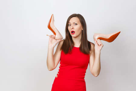 Attractive glamour caucasian fashionable young pensive perplexed brown-hair woman in red dress getting beige shoes with red sole of shopping isolated on white background. Copy space for advertisementの写真素材