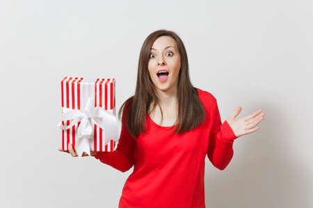Woman spreading hands, holding red striped present box with ribbon isolated on white background. For advertisement. St. Valentines Day, International Women's Day, Christmas, birthday, holiday conceptの写真素材