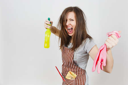 Young fun crazy loony wild screaming housewife tousled hair in apron squeegee rag in pocket isolated on white background. Mad woman shoot from spray bottle with cleaner liquid pink gloves. Copy spaceの写真素材