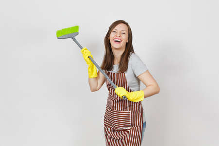 Young smiling housewife in striped apron, yellow gloves isolated on white background. Fun housekeeper woman cleaning maid holding and sweeping with broom Copy space for advertisement Advertising areaの写真素材