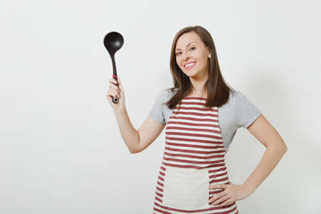 Young attractive smiling caucasian housewife in striped apron isolated on white background. Beautiful housekeeper woman holding black kitchen soup ladle. Copy space for advertisementの写真素材