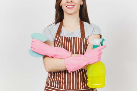 Close up cropped portrait housewife in pink gloves, striped apron isolated on white background. Woman holding hands crossed, spray bottle with cleaner liquid, sponge. Copy space for advertisementの写真素材