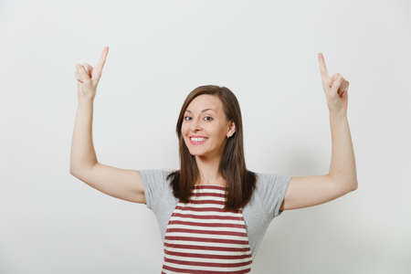 Closeup young attractive smiling brunette caucasian housewife in apron isolated on white background. Beautiful housekeeper woman pointing index fingers up looking camera. Copy space for advertisementの写真素材
