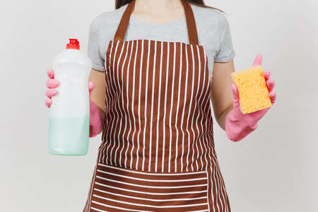 Close up cropped portrait housewife in pink gloves, striped brown apron isolated on white background. Woman holding bottle with cleaner liquid for washing dishes, sponge. Copy space for advertisementの写真素材