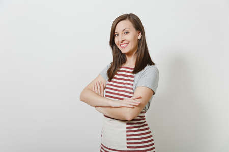 Portrait of young attractive smiling brunette caucasian housewife in striped apron isolated on white background. Beautiful housekeeper woman with folded arms looking camera for advertisementの写真素材