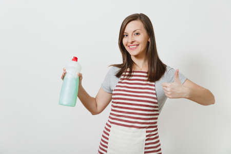 Housewife in striped apron looking camera isolated on white background. Housekeeper woman showing thumb up, holding bottle with dishwashing cleaner liquid. Bottle with copy space for advertisementの写真素材