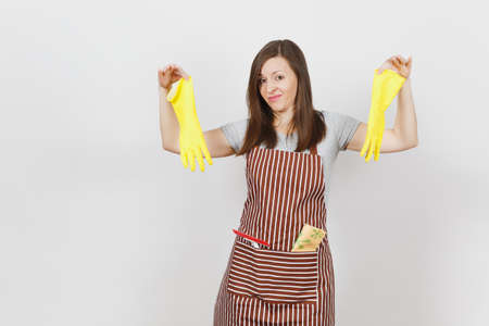 Young sad upset tired shocked housewife in striped apron with cleaning rag in pocket isolated on white background. Housekeeper woman holds smell yellow gloves in spreading hands. For advertisementの写真素材