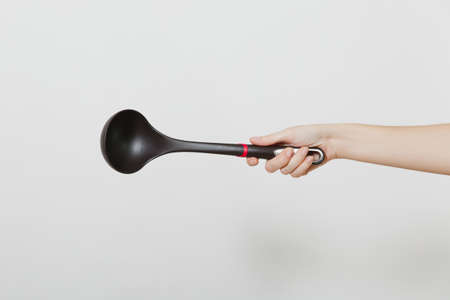 Close up of female hand horizontal holding black ladle dipper isolated on white background. Kitchen utensils concept. Copy space for advertisementの写真素材