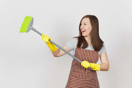 Young smiling housewife in striped apron, yellow gloves isolated on white background. Fun housekeeper woman cleaning maid holding and sweeping with broom Copy space for advertisement Advertising areaの写真素材