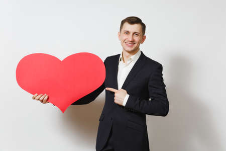 Young man in suit pointing index finger on big red heart isolated on white background. Copy space, advertisement. Place for text. St. Valentine's Day, International Women Day birthday holiday conceptの写真素材