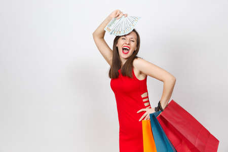 Attractive glamour fashionable young brown-hair woman in red dress holding cash dollars, multi colored packets with purchases after shopping isolated on white background. Copy space for advertisementの写真素材
