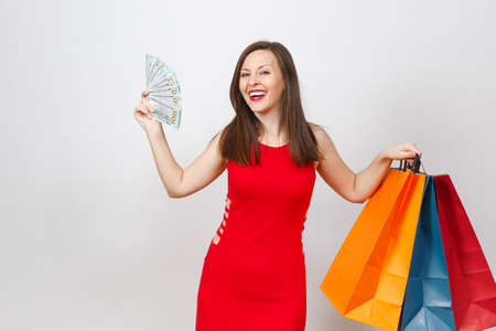 Attractive glamour fashionable young brown-hair woman in red dress holding cash dollars, multi colored packets with purchases after shopping isolated on white background. Copy space for advertisementの写真素材