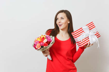 Young pretty woman in red clothes holding bouquet of beautiful roses flowers, present box with gift isolated on white background. St Valentines Day, International Women's Day birthday holiday conceptの写真素材