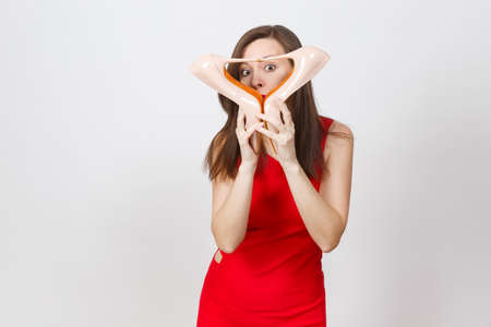 Attractive glamour fashionable young brown-hair woman in red dress putting heels to head, getting beige shoes with red sole of her shopping isolated on white background. Copy space for advertisementの写真素材