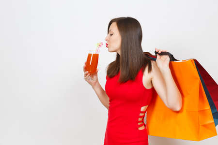 Attractive glamour fashionable young woman in red dress holding glass of drink cocktail, multi colored packets with purchases after shopping isolated on white background. Copy space for advertisementの写真素材