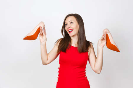 Attractive glamour caucasian fashionable young smiling brown-hair woman in red dress holding beige shoes with red sole of her shopping isolated on white background. Copy space for advertisementの写真素材