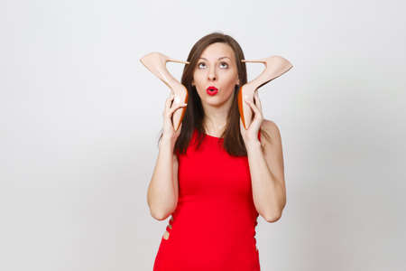 Attractive glamour fashionable young brown-hair woman in red dress putting heels to head, getting beige shoes with red sole of her shopping isolated on white background. Copy space for advertisementの写真素材