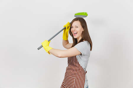 Young smiling housewife in striped apron, yellow gloves isolated on white background. Fun housekeeper woman cleaning maid holding and sweeping with broom Copy space for advertisement Advertising areaの写真素材