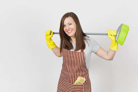 Young smiling housewife in striped apron, yellow gloves isolated on white background. Housekeeper woman cleaning maid holding and sweeping with broom. Copy space for advertisement. Advertising areaの写真素材