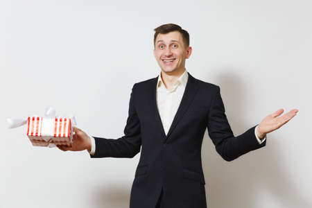 Young man in suit spreading hands, holding red present box with gift isolated on white background. Copy space for advertisement. St. Valentine's Day International Women's Day birthday holiday conceptの写真素材