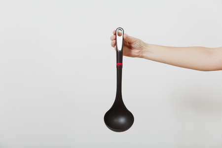 Close up of female hand vertical holding black ladle dipper isolated on white background. Kitchen utensils concept. Copy space for advertisementの写真素材
