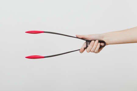 Close up of female hand horizontal holding black and red kitchen salat serving plastic pair of tongs isolated on white background. Kitchen utensils concept. Copy space for advertisementの写真素材