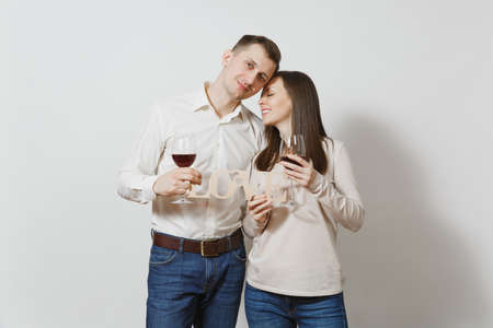 Young caucasian couple. Happy smiling man and woman in love in casual light clothes, jeans making toast, drinking from glasses of red wine isolated on white background. Copy space for advertisementの写真素材