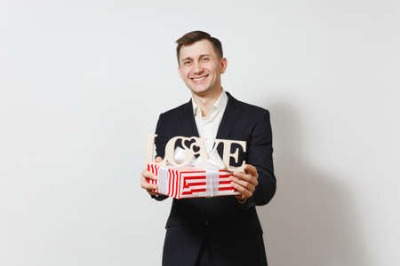 Young man in suit holding wooden word Love, red present box with gift isolated on white background. Copy space for advertisement. St. Valentines Day, International Womens Day birthday holiday conceptの写真素材