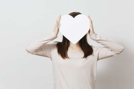 Young brunette woman holding big white heart in front face on white background. Copy space for...