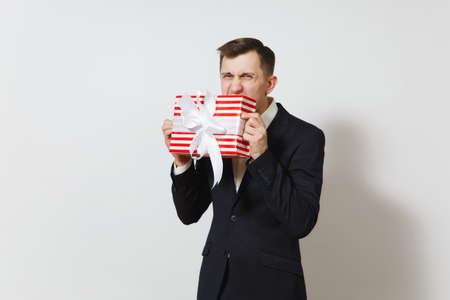 Young handsome fun man in suit biting red present box with gift isolated on white background. Copy space for advertisement. St. Valentine's Day, International Women's Day, birthday, holiday conceptの写真素材