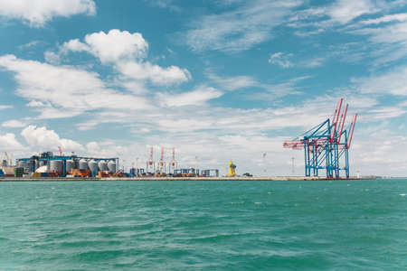 Beautiful seascape. Azure wavy restless sea with splashes and foam on background a cloudy blue sky on the horizon industrial large seaport on the shoreline.の写真素材