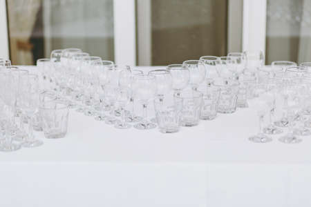 Preparing for party. Many clean shiny empty glasses for wine, champagne, whiskey, juice, water and other drinks on the table with white tablecloth for the party, event, celebration in the restaurant.の写真素材