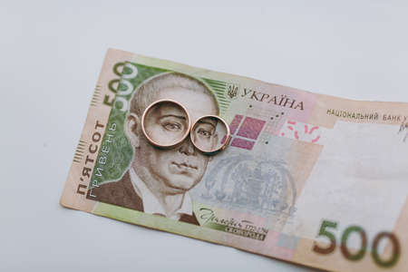 Close up Two beautiful stylish gold wedding rings of the bride and groom adjoin on a money bill portraying glasses on a white background. Wedding accessories, jewelry.の写真素材