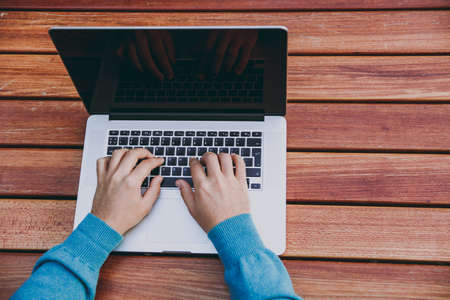 Close up cropped of hands on the keyboard. Successful smart man businessman or student sitting at table with mobile phone in city park using laptop, working outdoors. Mobile Office concept. Top viewの写真素材