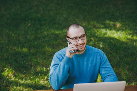 Young successful smiling smart man businessman or student in casual blue shirt, glasses sitting at...