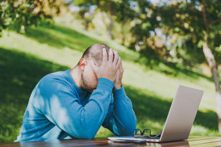 Young tired sad man businessman or student in casual blue shirt, glasses sitting at table with...