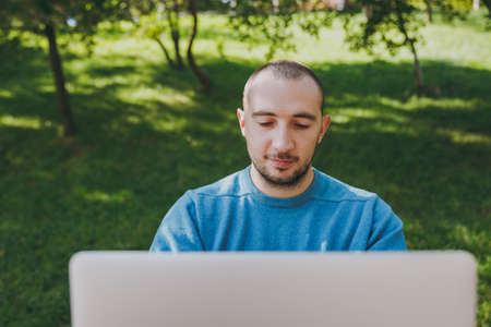 Close up young successful smart man businessman or student in casual blue shirt, sitting at table in city park using laptop, working outdoors. Mobile Office concept. Copy space for advertisementの写真素材