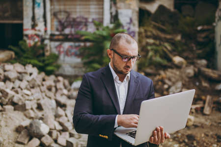 Young successful smart businessman in white shirt, classic suit, glasses. Man standing and working...