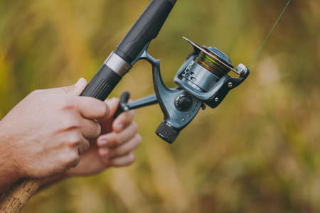 Close up A man holds and untwists a fishing reel in his hands on a blurry brown background. Lifestyle, recreation, fisherman leisure concept. Copy space for advertisement. With place for textの写真素材