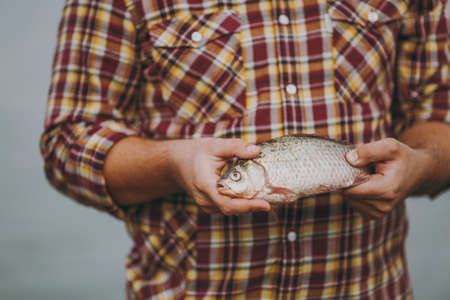 Close up A man in checkered shirt holds in his hands a fish with an open mouth on a blurred gray background. Lifestyle, recreation, leisure concept.の写真素材