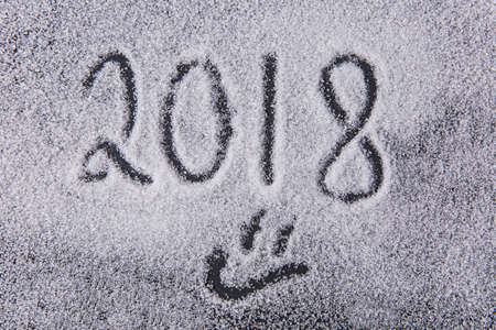 Written by a finger number 2018 and smiley on the texture of white sugar crystals on the black backgroundの写真素材