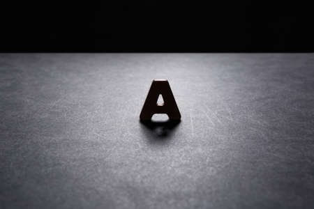 Wooden letter A on the dark texture with a black background with backlight. Lighting effect.の写真素材