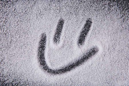 Written by a finger smiley icon on the texture of white sugar crystals on the black background