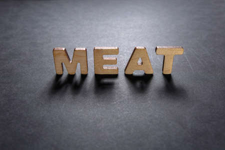 Word Meat of wooden letters on the dark texture with a black background with backlight. Lighting...