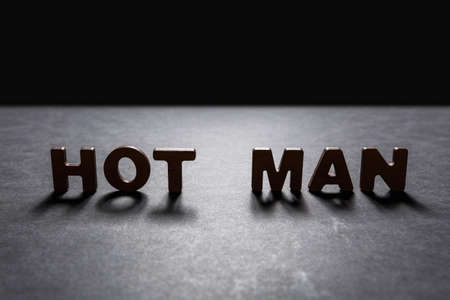 Word Hot man of wooden letters on the dark texture with a black background with backlight. Lighting effect.の写真素材