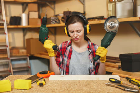 Young brown-hair woman in plaid shirt, gray T-shirt, noise insulated headphones, yellow gloves...