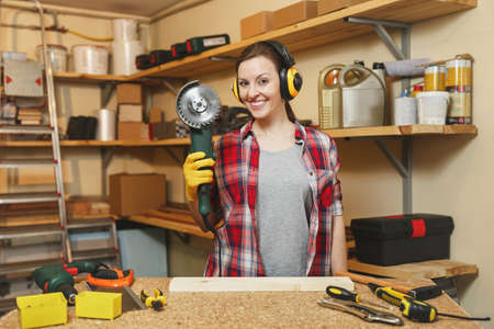 Pretty caucasian young brown-hair woman in plaid shirt, gray T-shirt, noise insulated headphones,...
