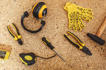 Top view working tool: noise insulated headphones, tape measure, yellow gloves, wrench, screwdrivers, hammer, pliers, nippers close-up on wooden texture table. Flat lay copy space for advertisementの写真素材